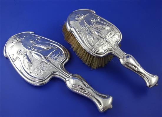 An Edwardian Art Nouveau repousse silver hand mirror and matching brush, mirror 11.5in.